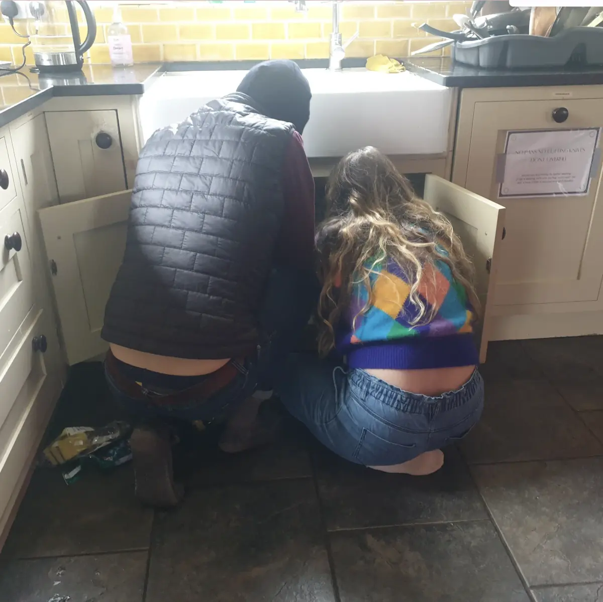 Two colivers crouched at the kitchen sink, fixing the plumbing together